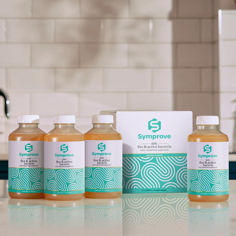 Four bottles of Symprove Live & Active Water-Based Food Supplement placed in a row on a kitchen countertop, with packaging in the background.